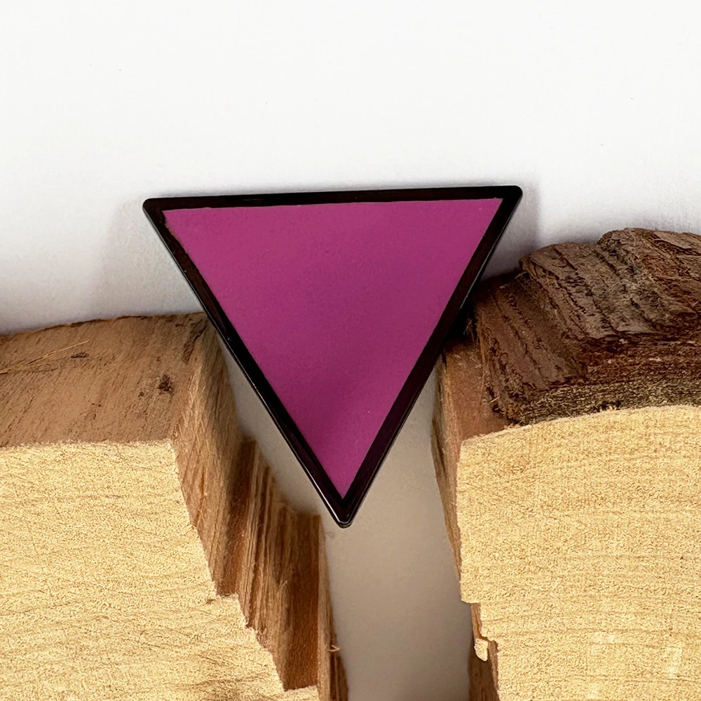 Pin’s triangle rose Pride présenté sur bois